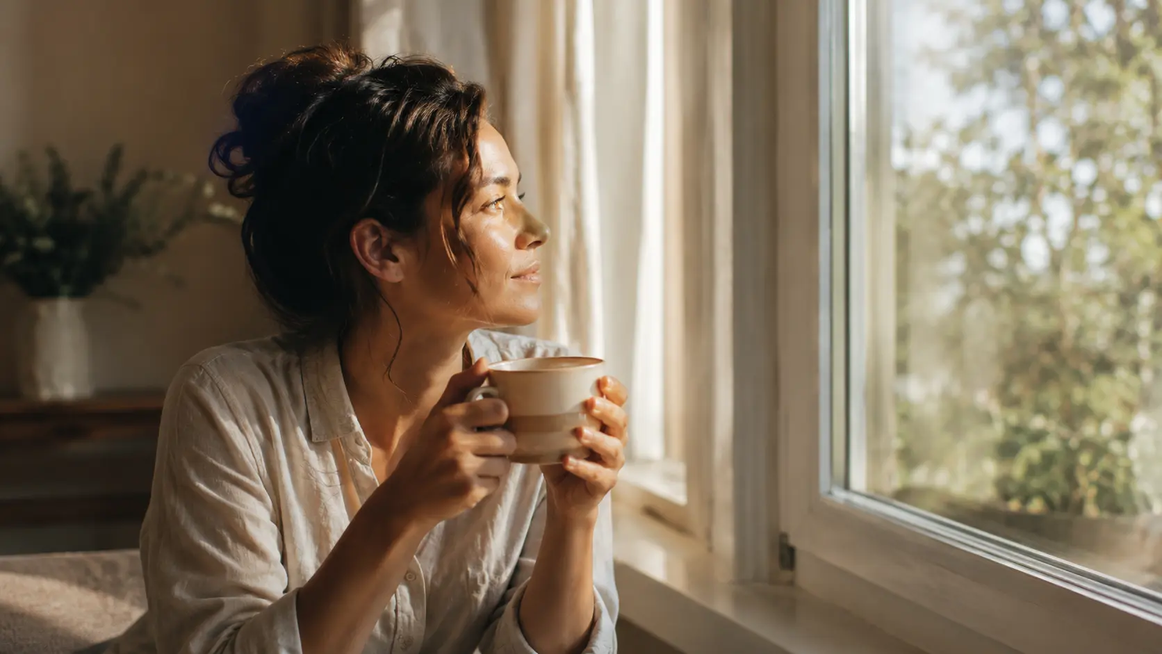 Woman sitting by a sunlit window in quiet reflection, thinking about how to move on from the past